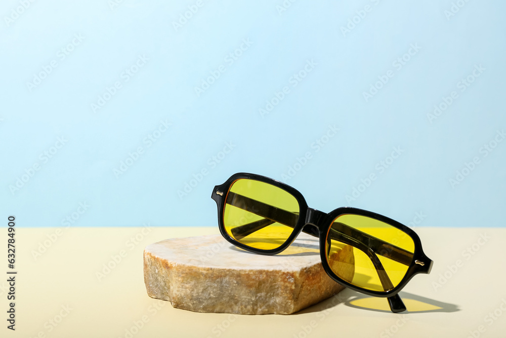 Stone with stylish sunglasses on yellow table