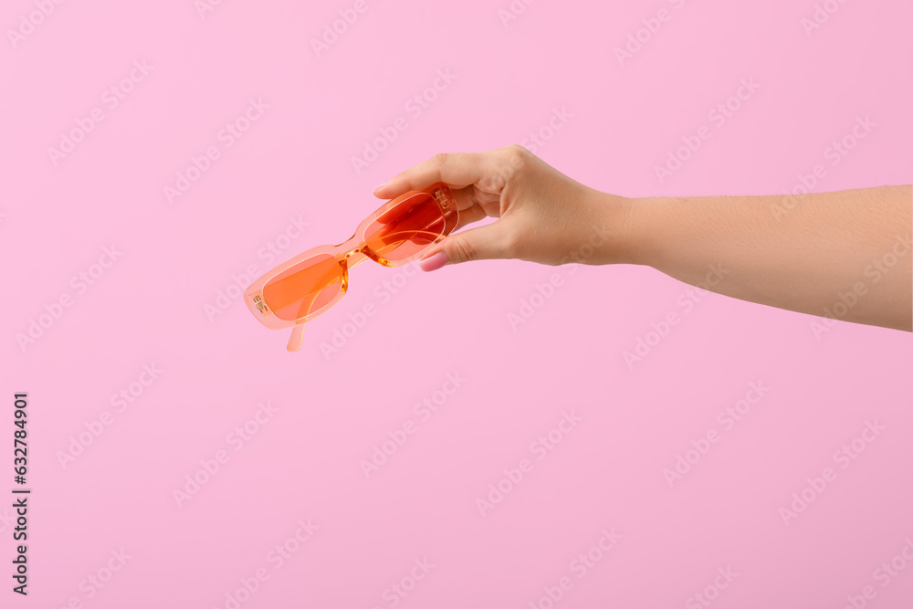 Woman holding stylish sunglasses on pink background