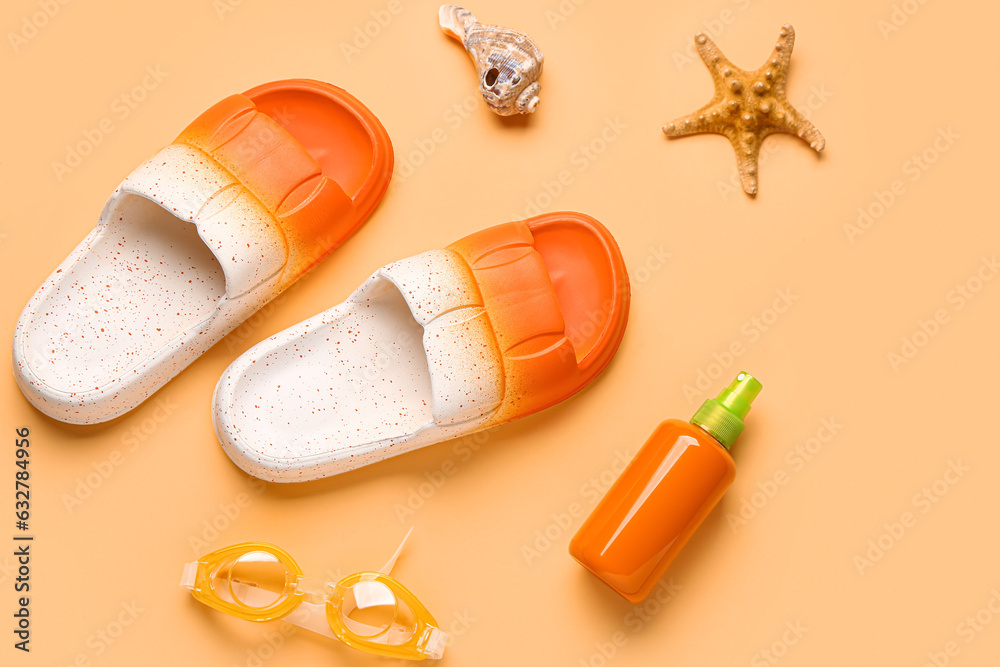 Female stylish flip flops, sunscreen cream and goggles on orange background