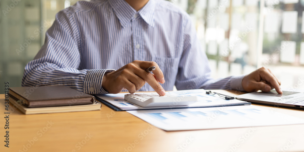 Businessman working with laptop and analyzing charts on financial documents with calculator.