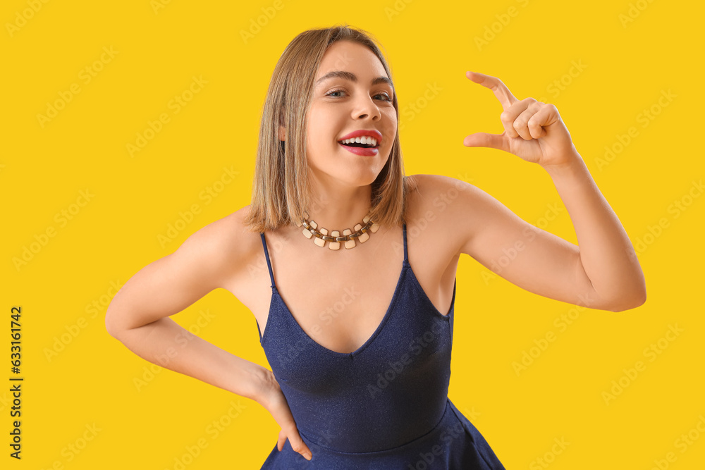 Young woman with necklace holding something on yellow background