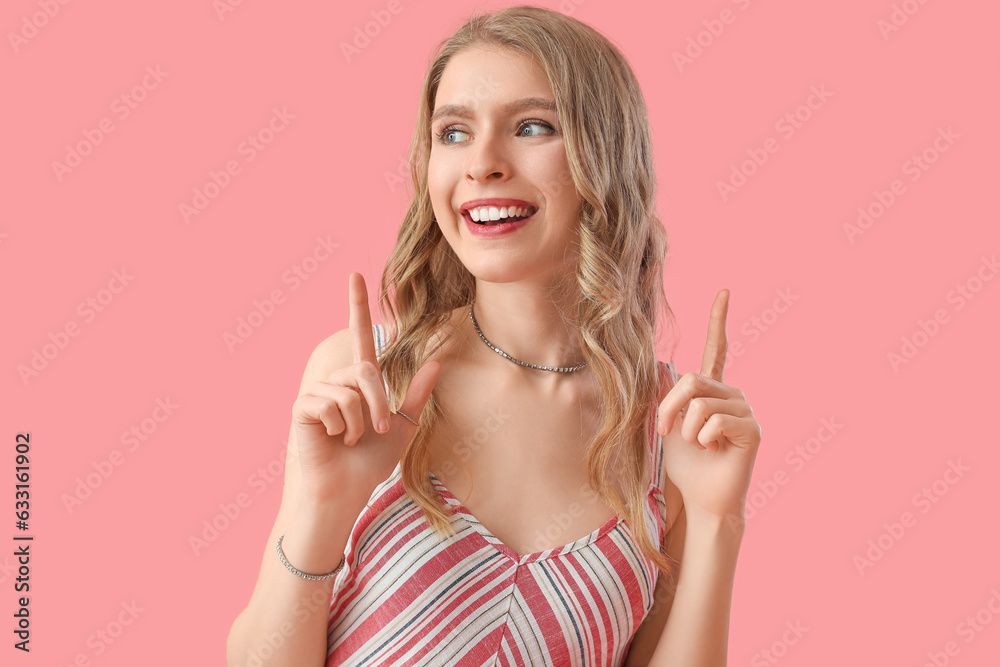 Young woman pointing at something on pink background