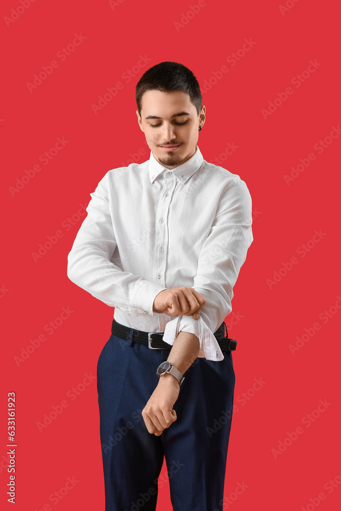 Young businessman rolling up his sleeve on red background