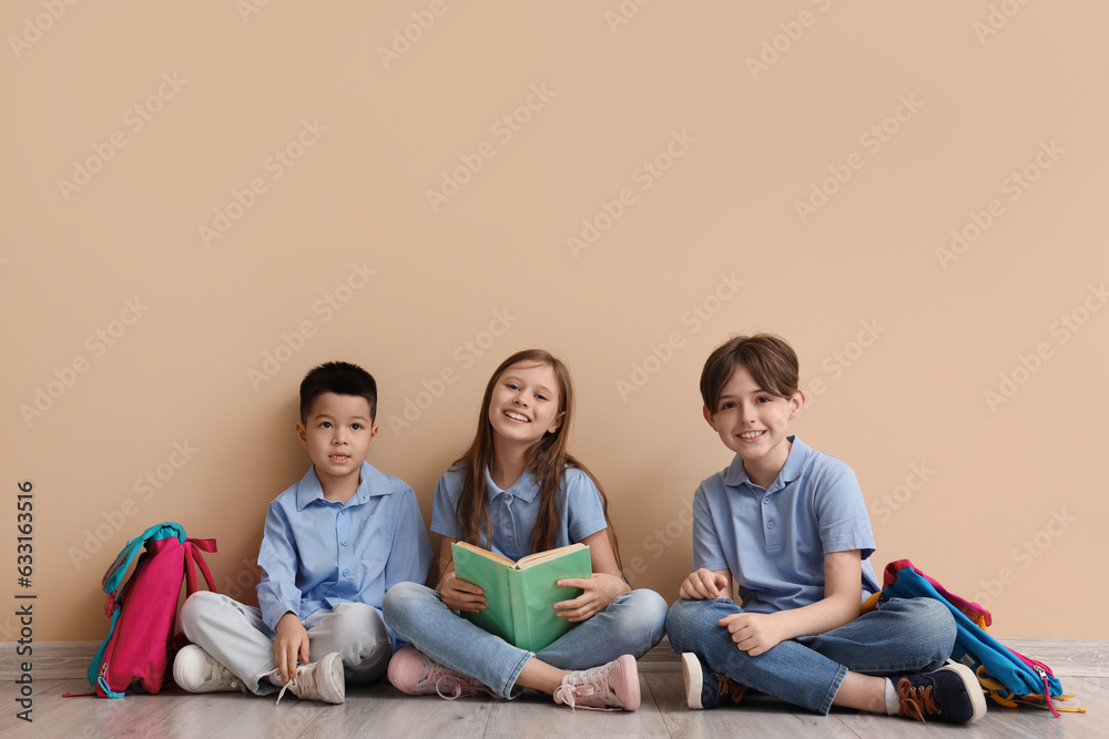 Little pupils reading book near beige wall