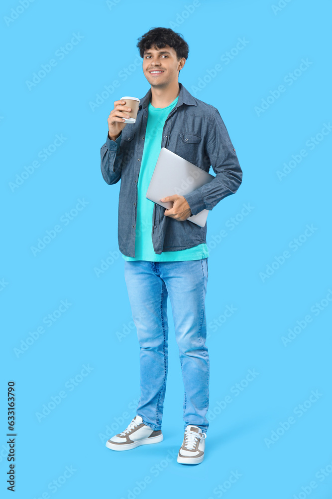 Male programmer with cup of coffee and laptop on blue background