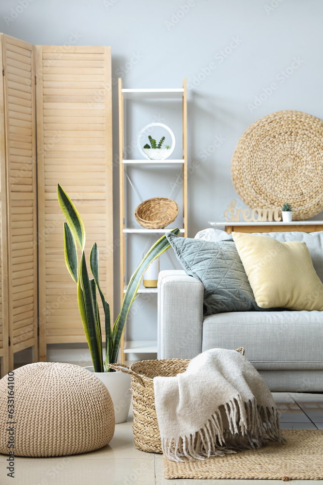 Cozy grey sofa and basket with soft blanket in interior of light living room