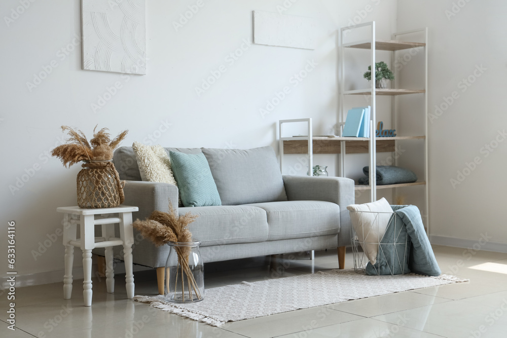 Cozy grey sofa and basket with soft blanket in interior of living room