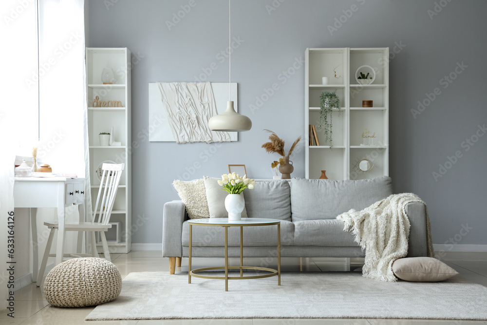 Cozy grey sofa with soft blanket and table in interior of light living room