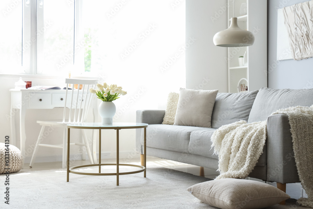 Cozy grey sofa with soft blanket and coffee table in interior of light living room