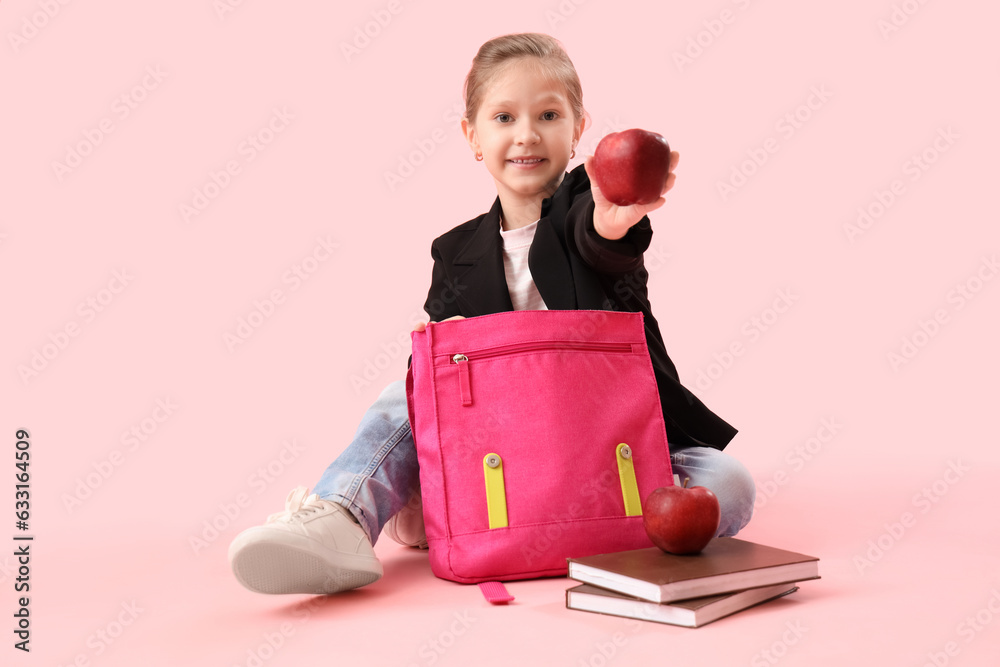 Little schoolgirl with backpack, books and apple on pink background