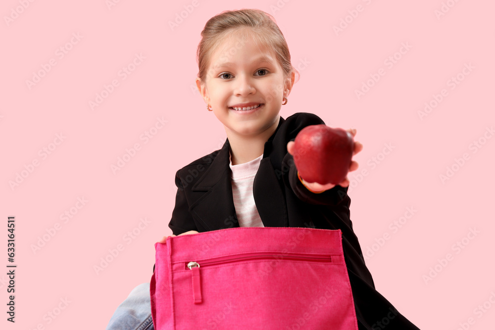 Little schoolgirl with backpack and apple on pink background