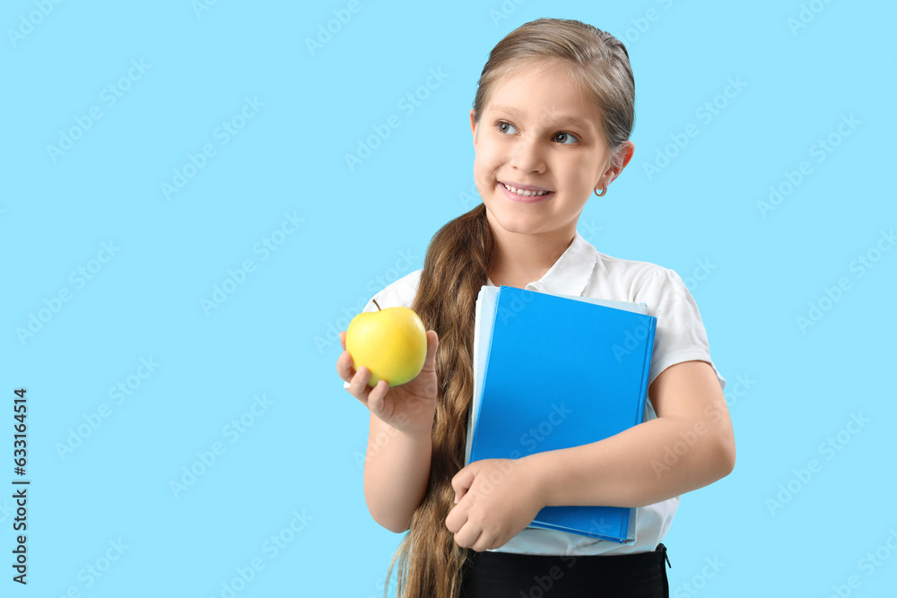 Little schoolgirl with book and apple on light blue background