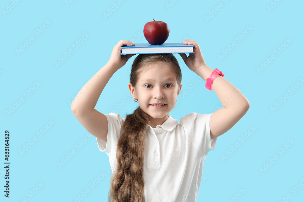 Little schoolgirl with book and apple on light blue background