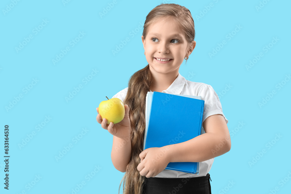 Little schoolgirl with book and apple on light blue background