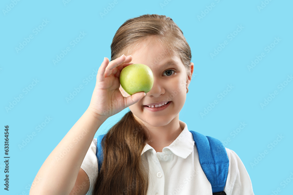 Little schoolgirl with apple on light blue background