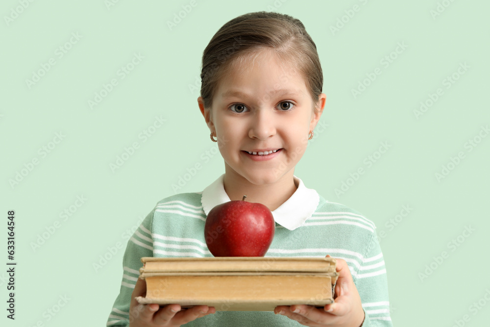 Little schoolgirl with books and apple on mint background