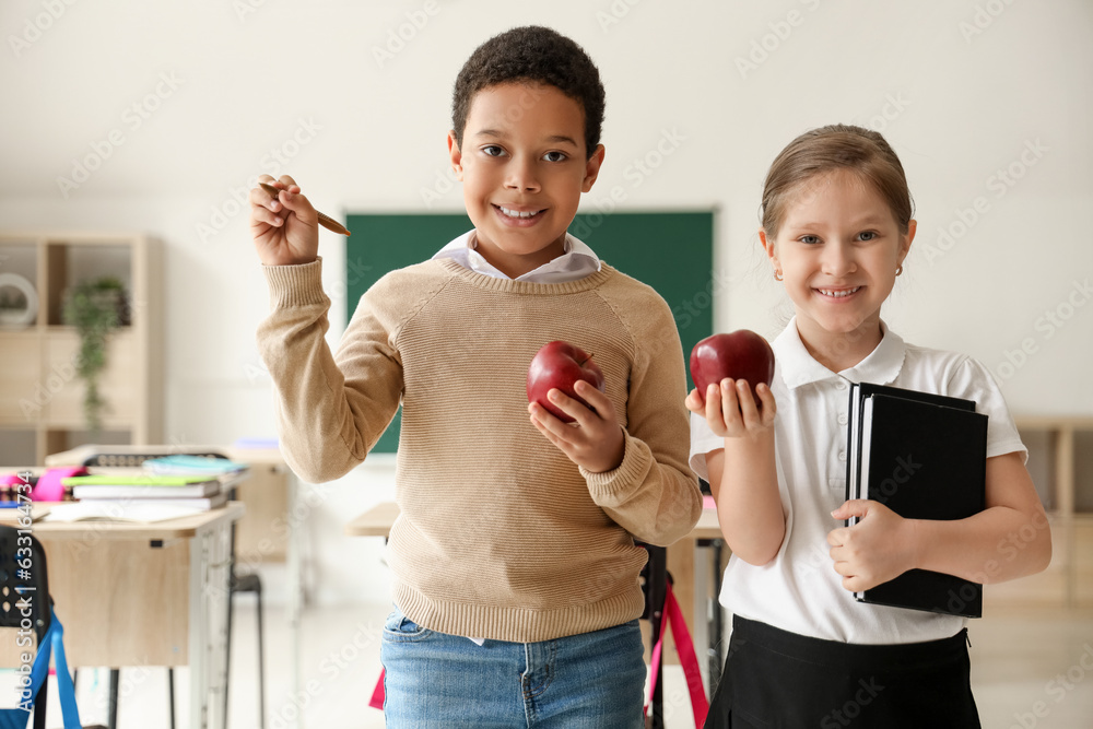 Little students with apples, pen and books in classroom