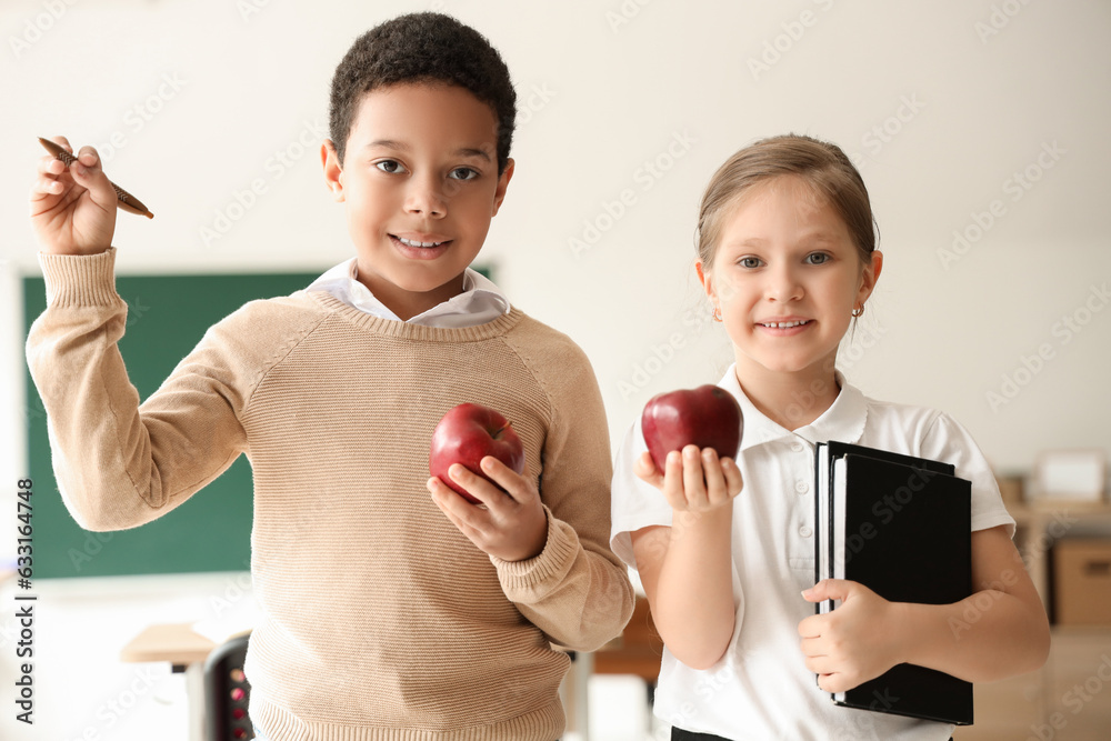 Little students with apples, pen and books in classroom