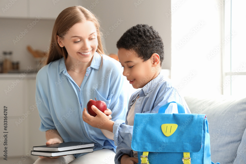 Woman helping her little son to pack schoolbag at home