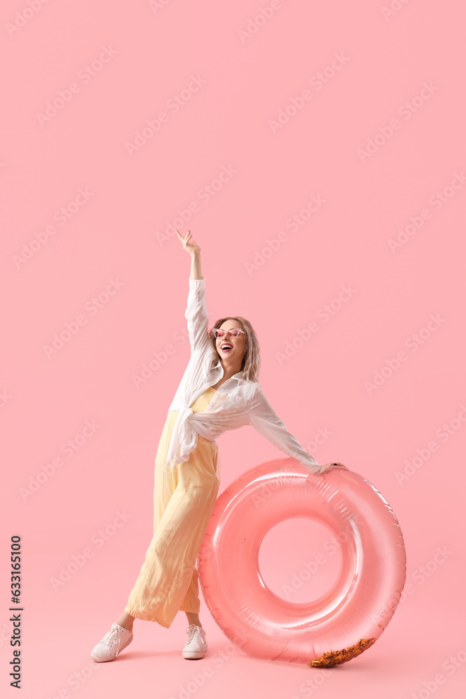 Young woman in sunglasses with inflatable ring on pink background