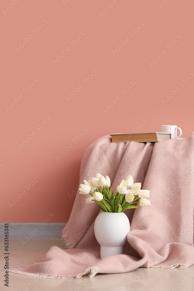 Plaid with book, cup and tulips in vase near pink wall