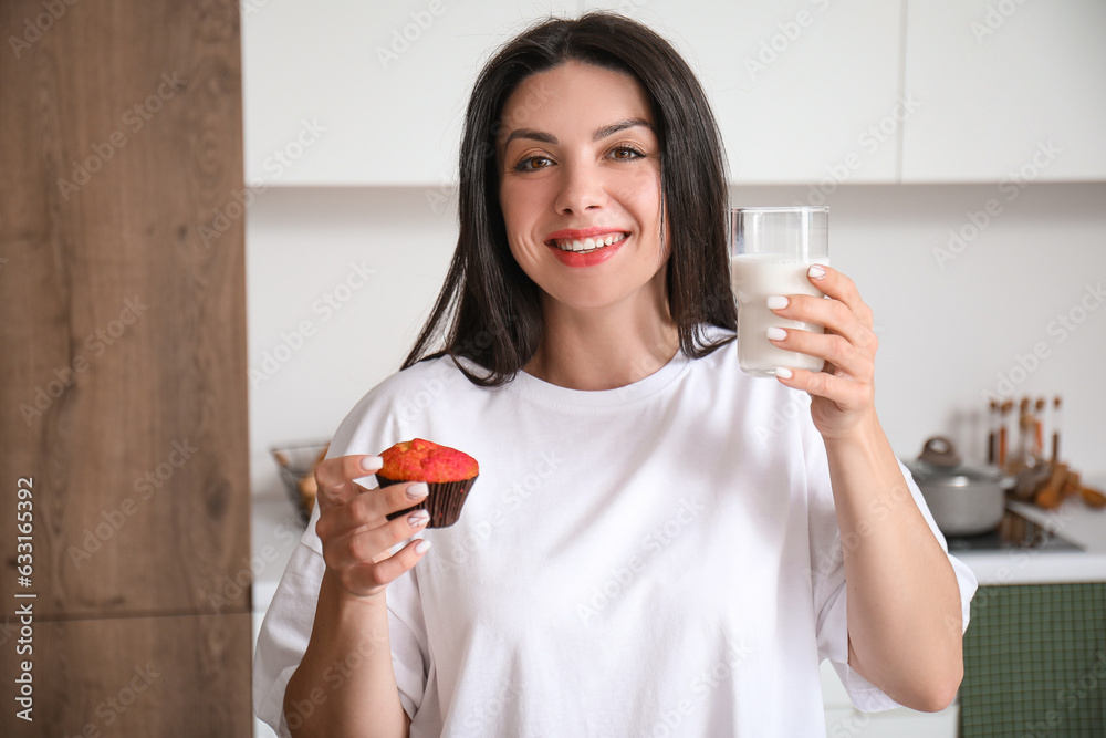 Beautiful woman with tasty muffin and glass of milk in kitchen