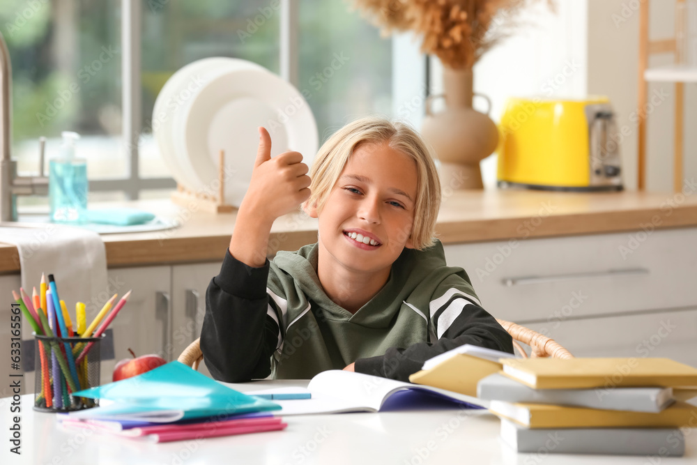 Little boy showing thumb-up while doing homework in kitchen