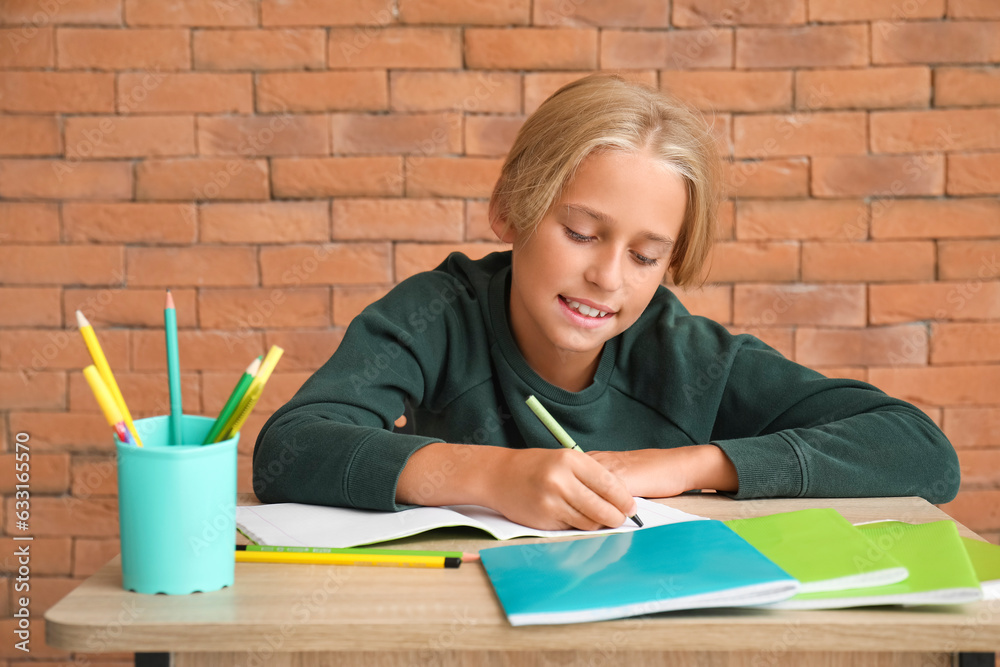 Little boy doing homework at table near brick wall