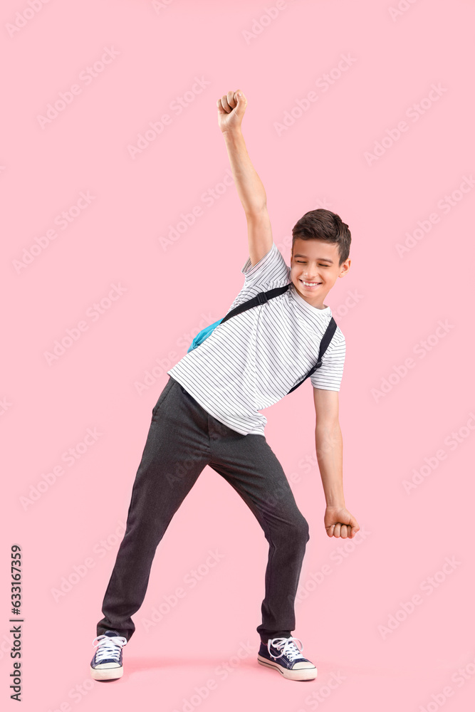 Portrait of schoolboy with backpack dancing on pink background