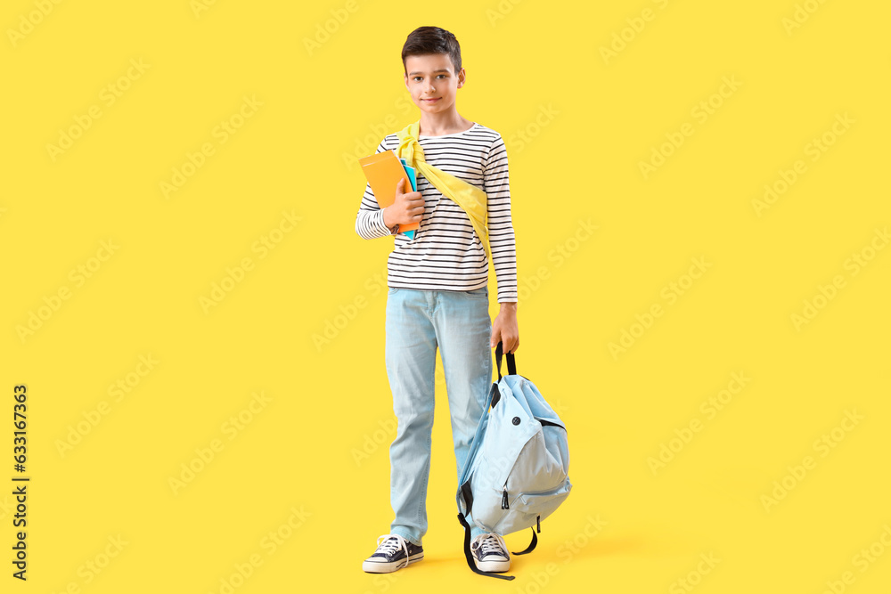 Portrait of schoolboy with backpack and school supplies on orange background