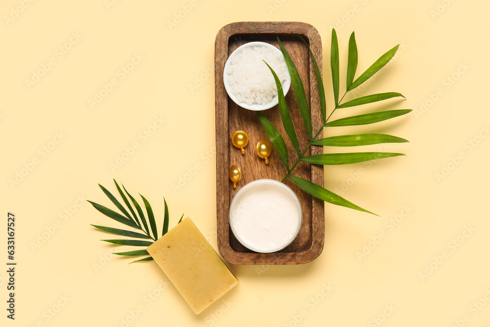 Wooden board with cosmetic products and palm leaves on color background