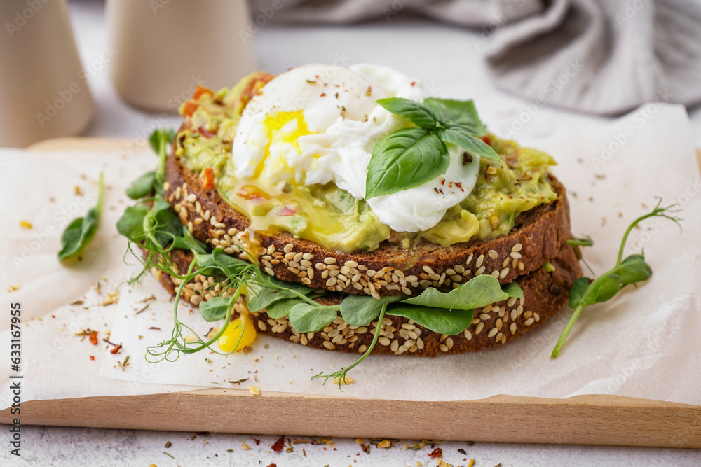 Wooden board of tasty sandwich with egg on light background