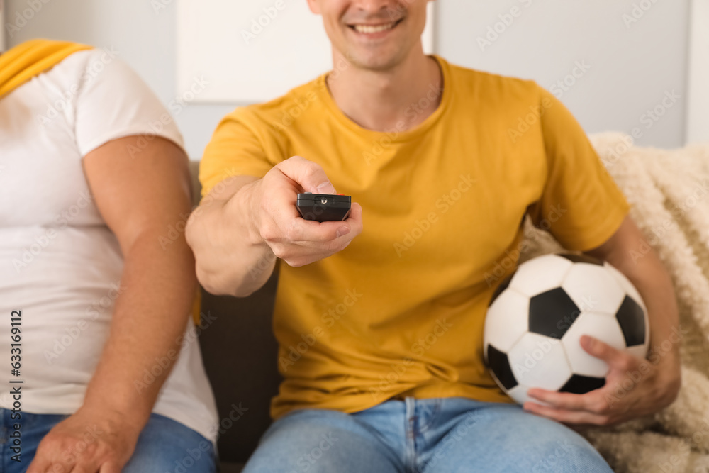 Young man with his father watching football game at home, closeup