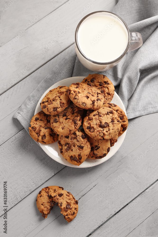 Cup of milk and tasty cookies with chocolate chips on grey wooden background