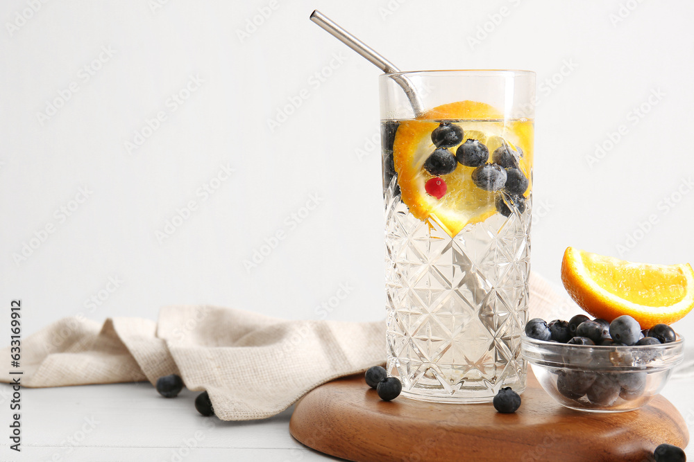 Glass of fresh blueberry lemonade and bowl with berries on white wooden table