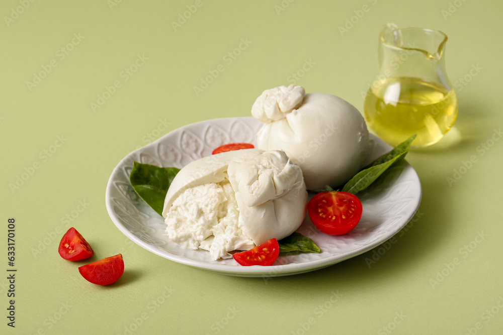 Plate of tasty Burrata cheese with basil and tomatoes on green background