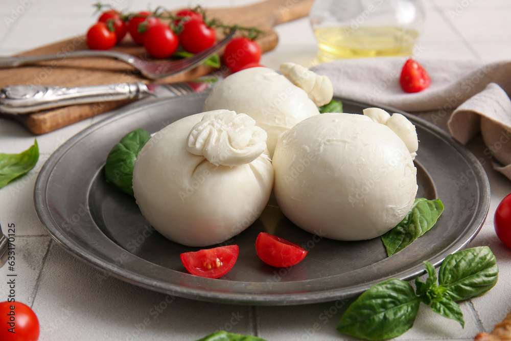 Plate of tasty Burrata cheese with basil and tomatoes on white tile table