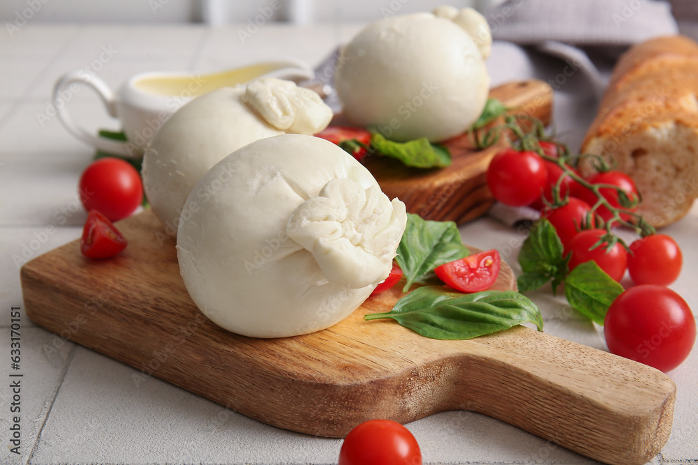 Wooden boards of tasty Burrata cheese with basil and tomatoes on white tile table