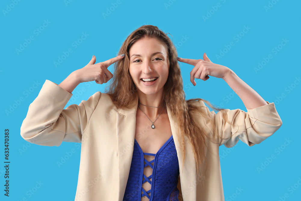 Beautiful young woman in jacket pointing at her head on blue background