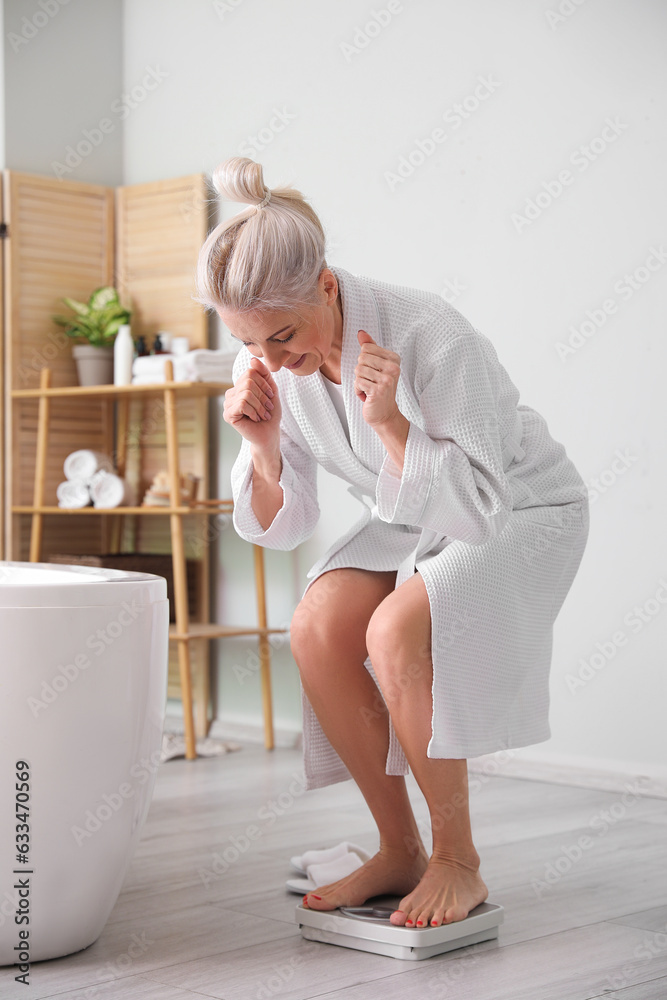 Mature woman measuring her weight on scales in bathroom