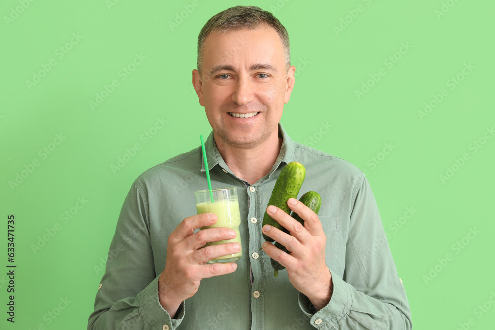 Mature man with glass of vegetable smoothie and cucumbers on green background