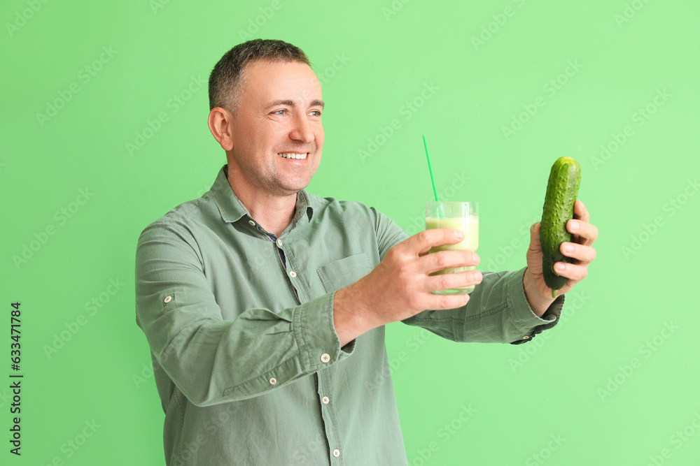 Mature man with glass of vegetable smoothie and cucumbers on green background