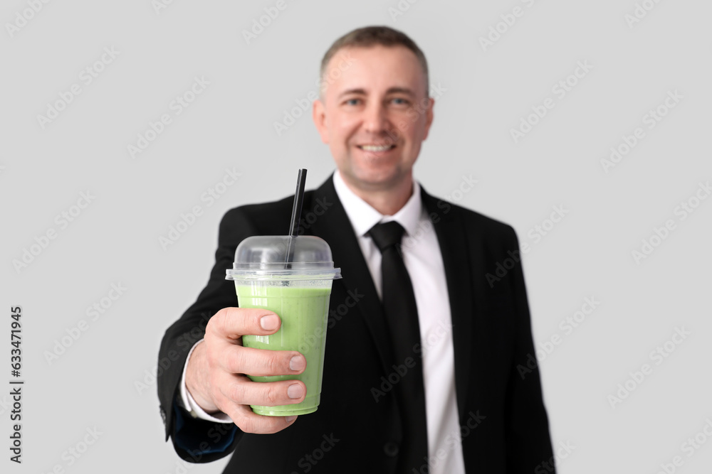 Mature businessman with glass of vegetable smoothie on light background