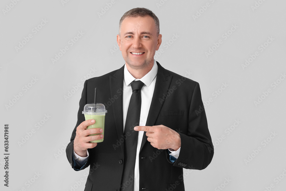 Mature businessman pointing at glass of vegetable smoothie on light background