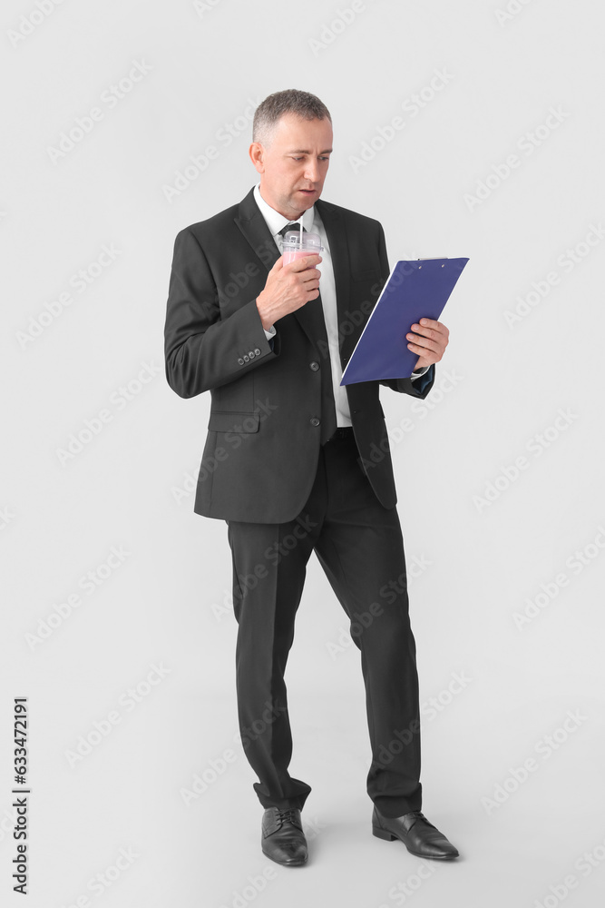 Mature businessman with glass of fruit smoothie and clipboard on light background