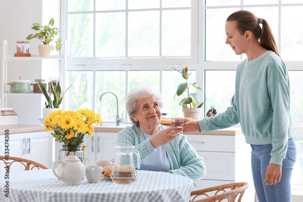 Senior woman taking glass of water from her granddaughter in kitchen