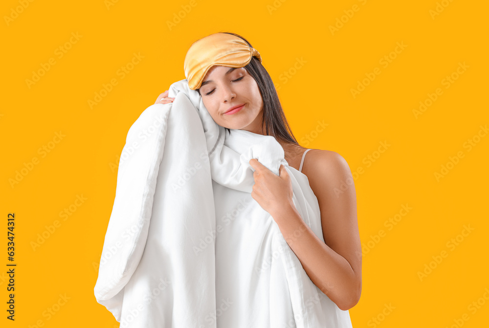 Young woman with sleeping mask and blanket on yellow background