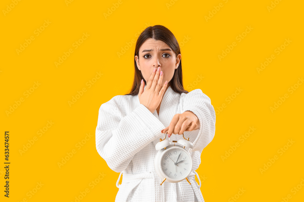 Shocked young woman with alarm clock on yellow background