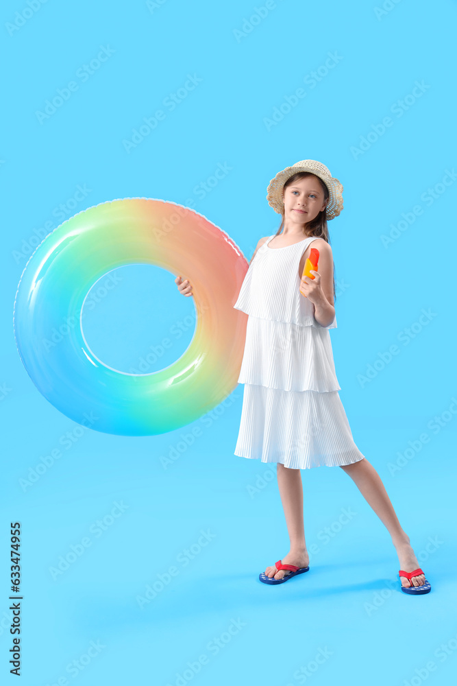 Little girl with bottle of sunscreen cream and inflatable ring on blue background