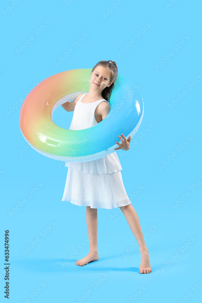 Little girl with inflatable ring and sunscreen cream on her face against blue background